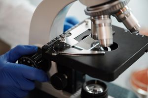 Close-up image of a scientist's gloved hand adjusting a microscope in a research lab.